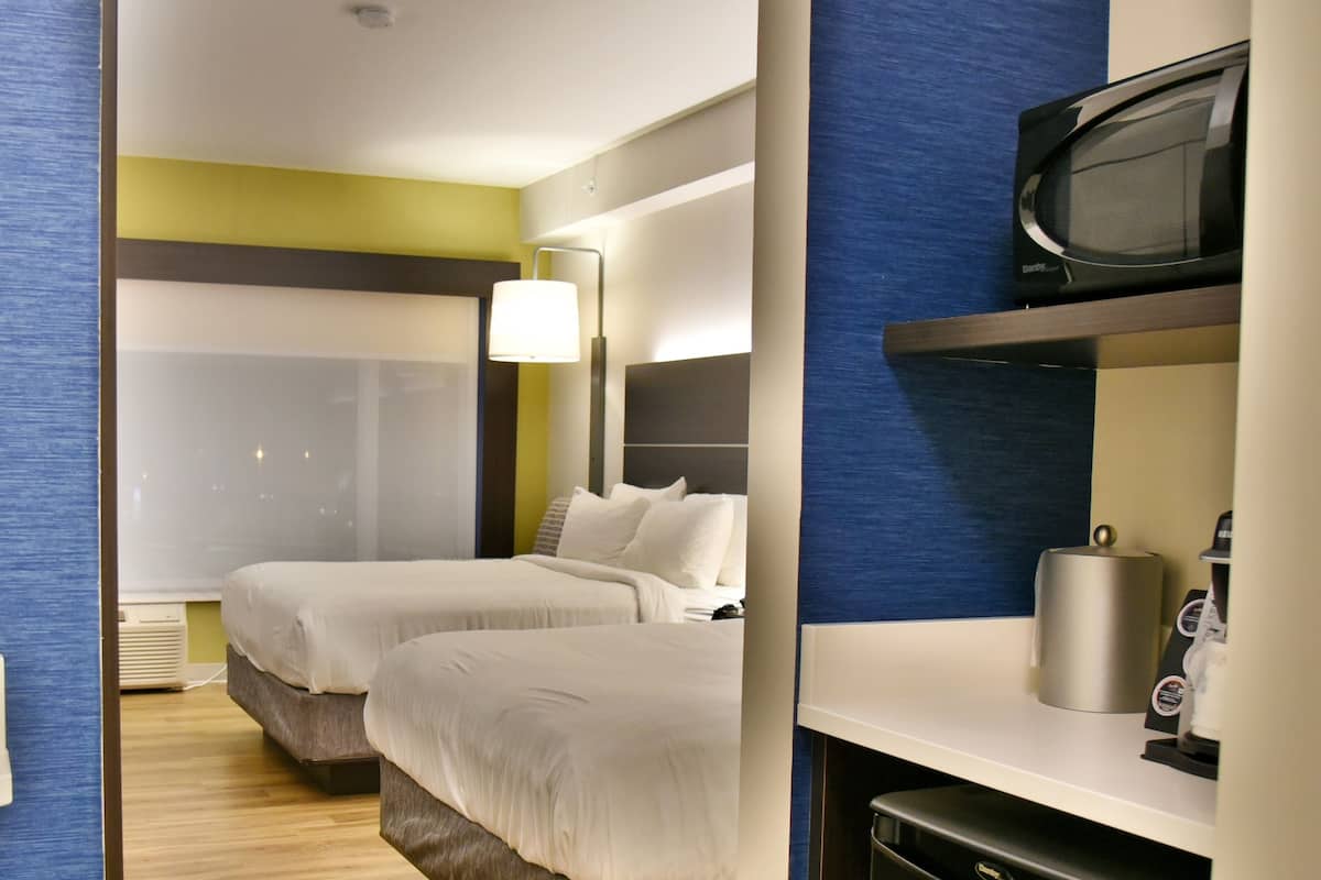 A hotel room with two beds, a television, a coffee machine, and a shower area.