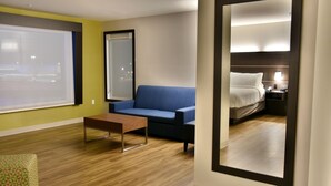 Una habitación de hotel con un ventanal grande, un sofá azul, una mesa de centro de madera y una cama con una mesita de noche.