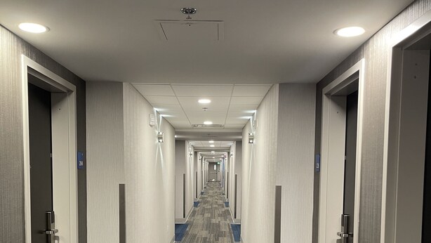 Hotellin käytävä, jossa on matto lattialla, ovet molemmin puolin ja upotetuilla valaisimilla varustettu katto.
