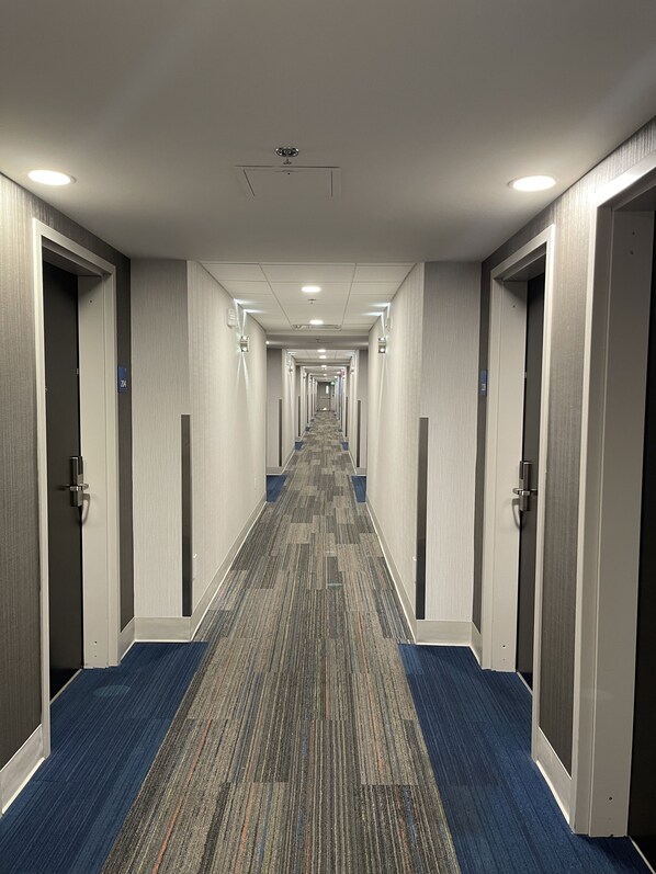 Un pasillo de hotel con pisos alfombrados, puertas a ambos lados y un techo con iluminación empotrada.