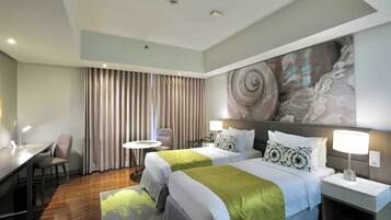 Habitación de hotel con dos camas, un escritorio, una silla, una mesa redonda y un cuadro abstracto grande en la pared.