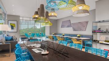 A modern dining area with a long wooden table, blue and yellow chairs, and geometric pendant lighting.