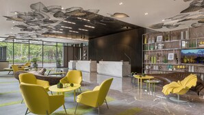 Un hall d’entrée moderne avec des chaises jaunes, un comptoir d’accueil et un plafond décoratif.