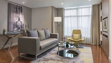 A modern living room with a grey sofa, a yellow armchair, a glass coffee table, and a large window with curtains.