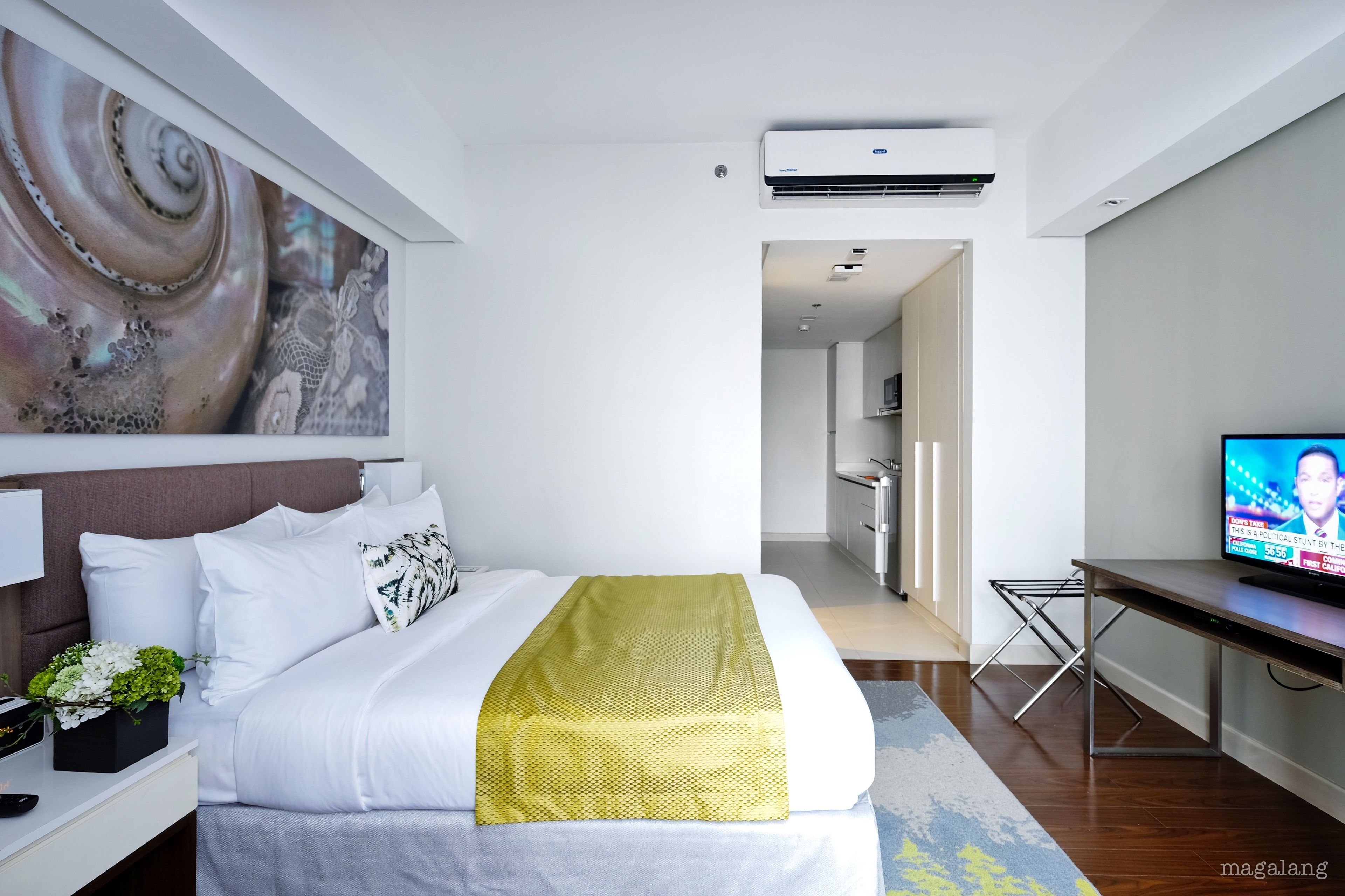 Ein modernes Hotelzimmer mit einem ordentlich bezogenen Bett, einem Flachbildfernseher und einem großen, abstrakten Gemälde an der Wand.