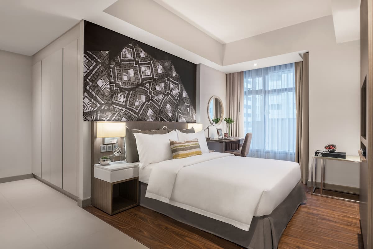 A modern hotel room with a large bed, a desk, a chair, and a large abstract artwork on the wall.