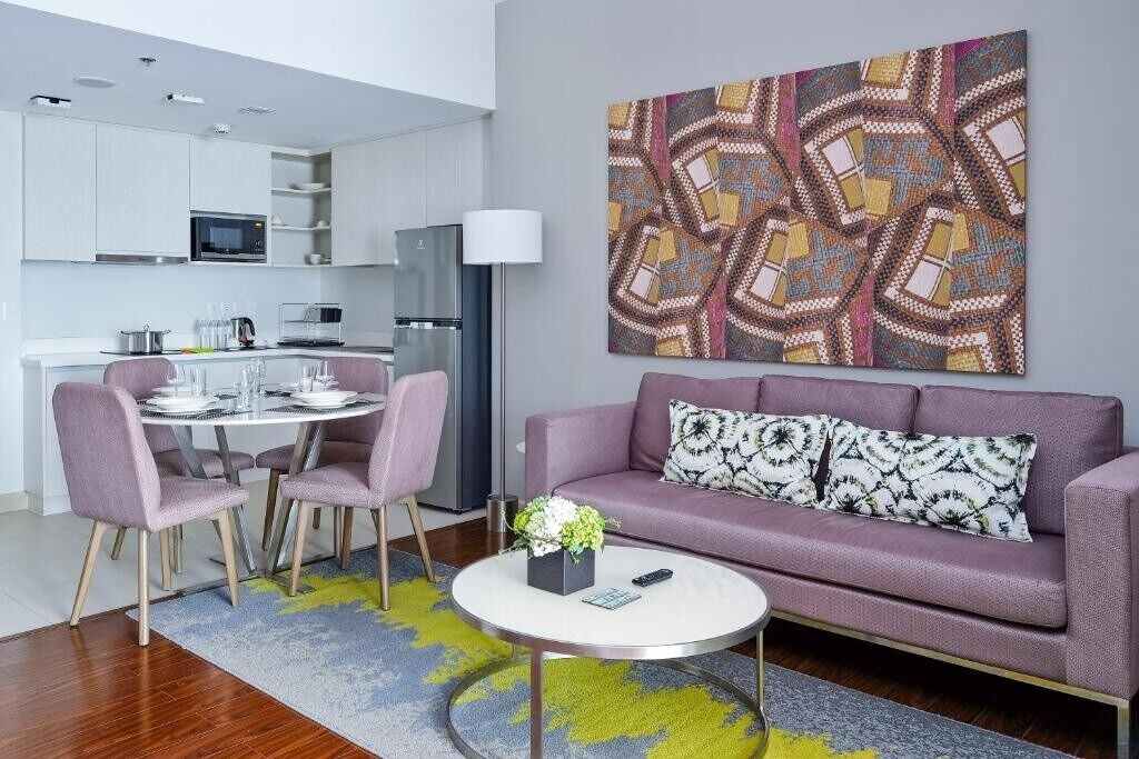 Una sala de estar moderna con un sofá púrpura, una mesa de centro redonda y una zona de comedor con una mesa y sillas blancas.