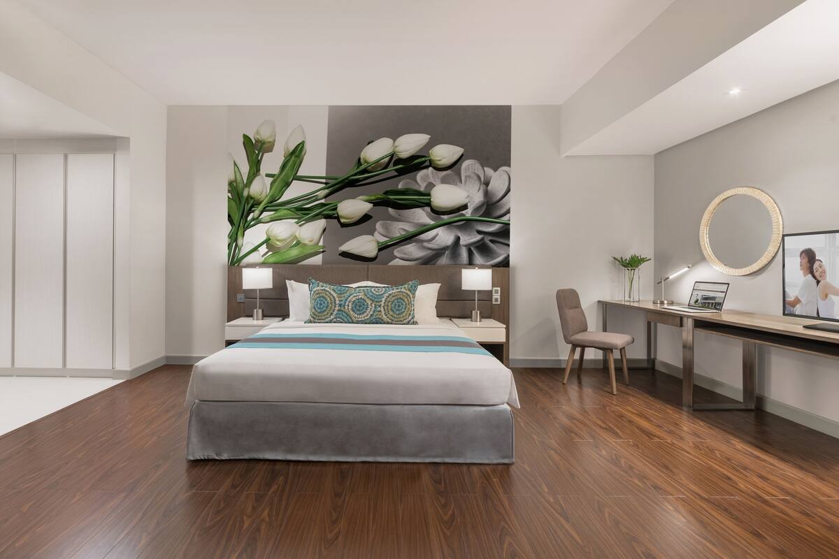 A modern hotel room with a large bed, a desk with a laptop, a chair, and a wall with a floral mural.