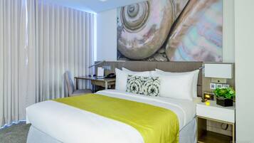 Una habitación de hotel con una cama grande, un escritorio y una mesita de noche con lámpara y planta.