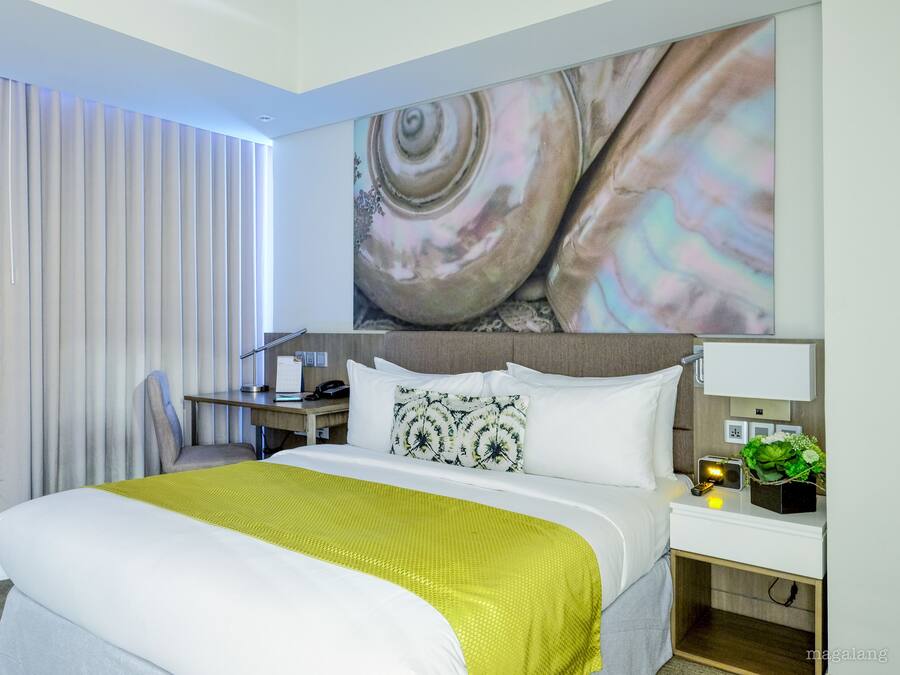 Una habitación de hotel con una cama grande, un escritorio y una mesita de noche con lámpara y planta.
