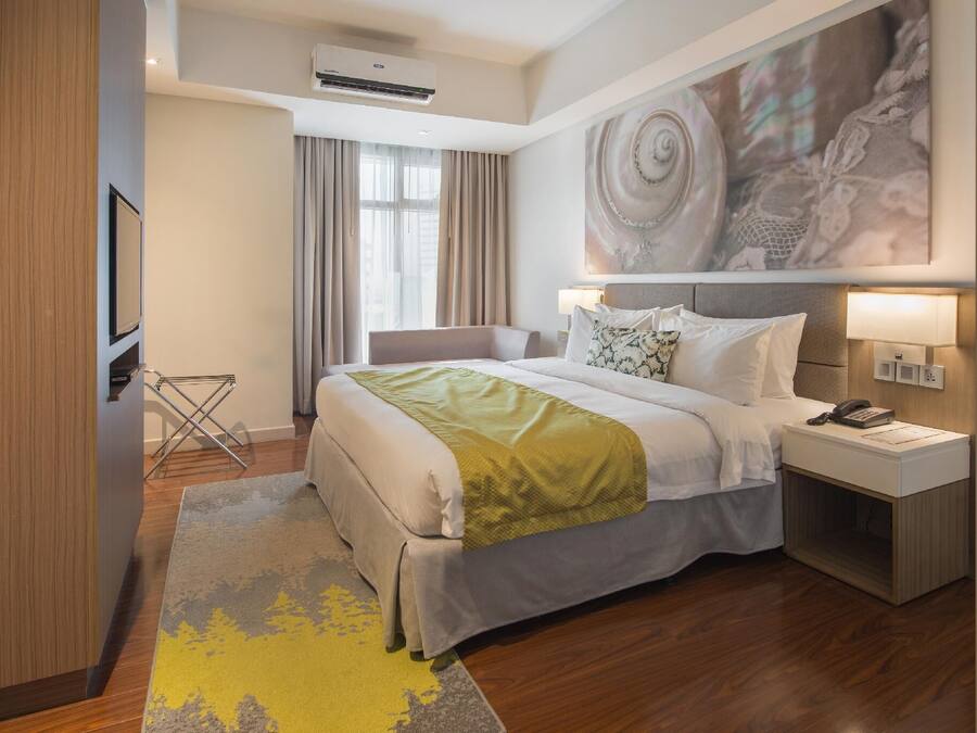 A hotel room with a bed, bedside table, lamp, and a large abstract painting on the wall.