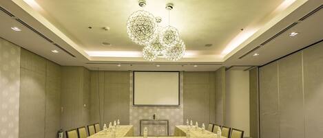 A conference room with a long table, multiple chairs, a projector screen, and a decorative chandelier.