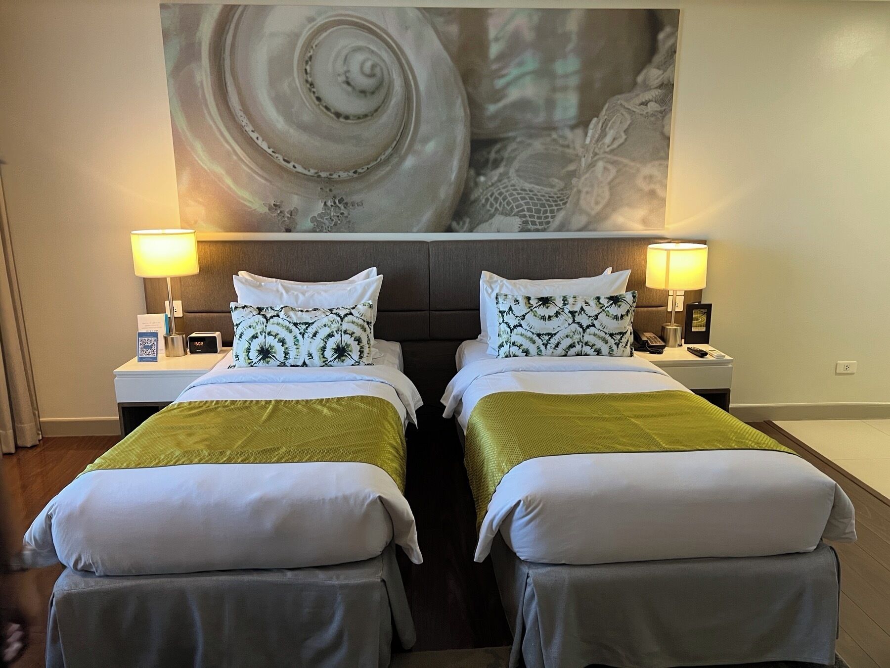 A hotel room with two beds, each with a nightstand, a lamp, and a wall-mounted artwork.