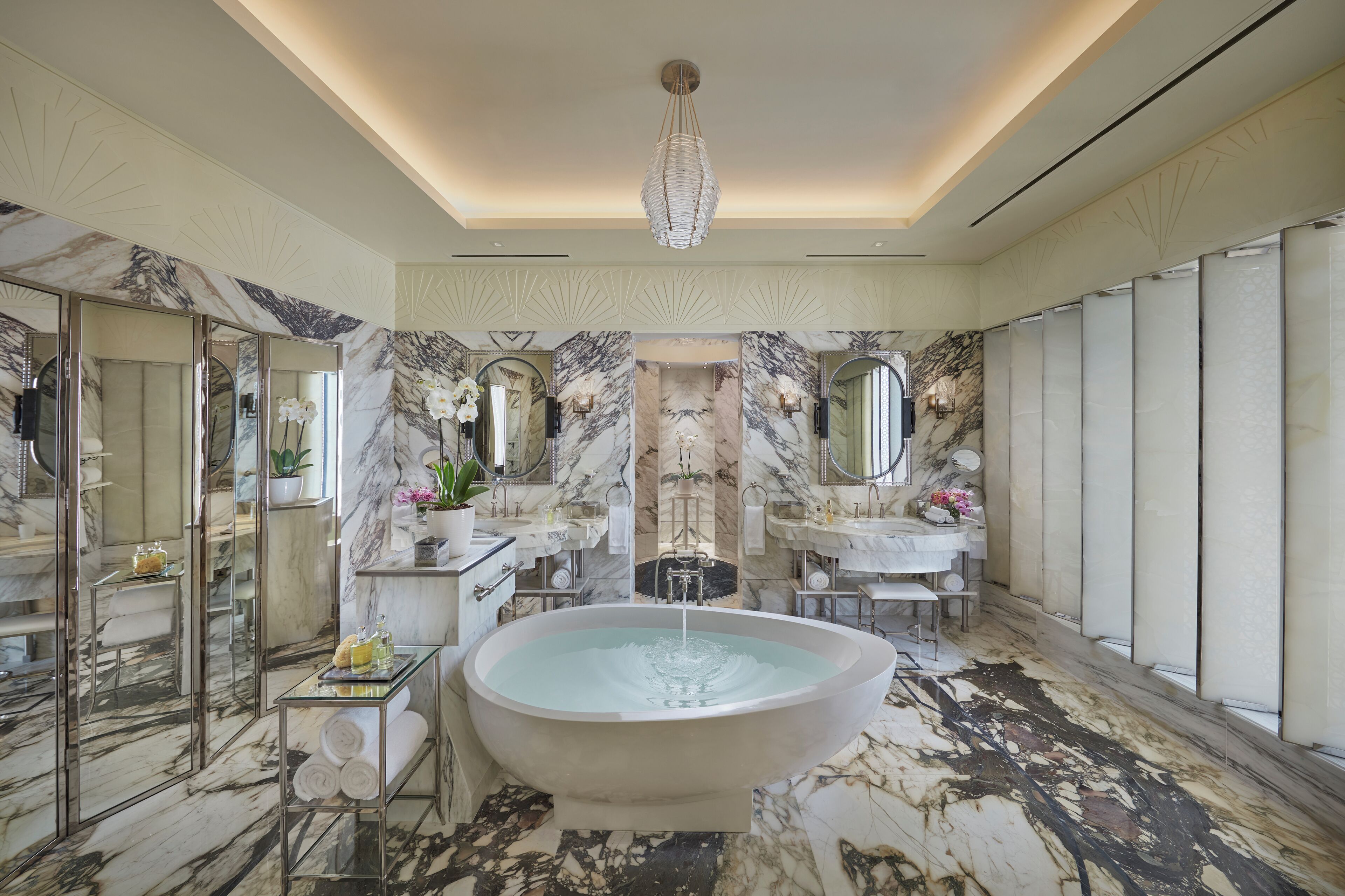 A luxurious bathroom with a freestanding bathtub, marble walls, and multiple mirrors.