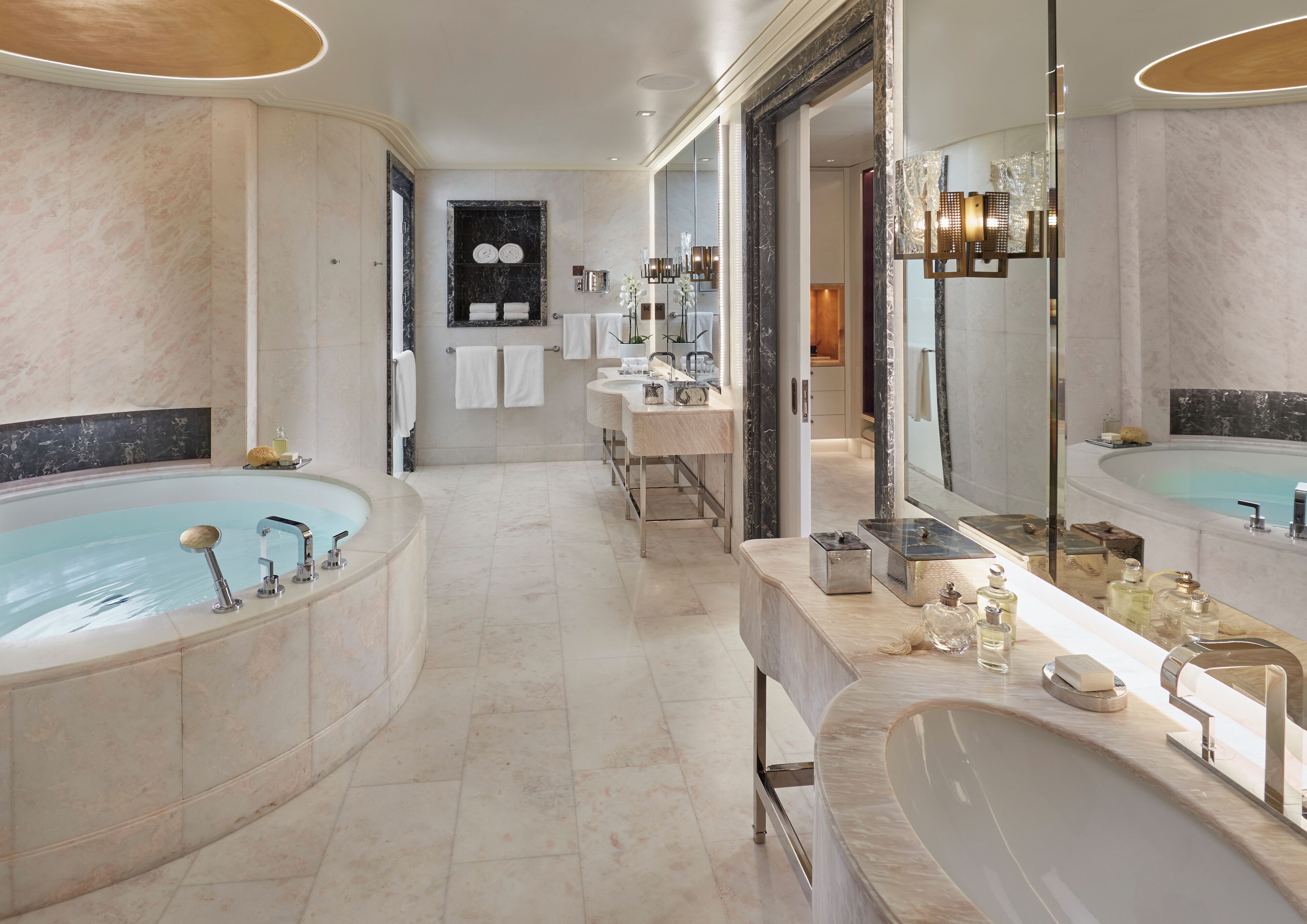 A luxurious bathroom with two large tubs, a vanity with a mirror, and a marble floor.