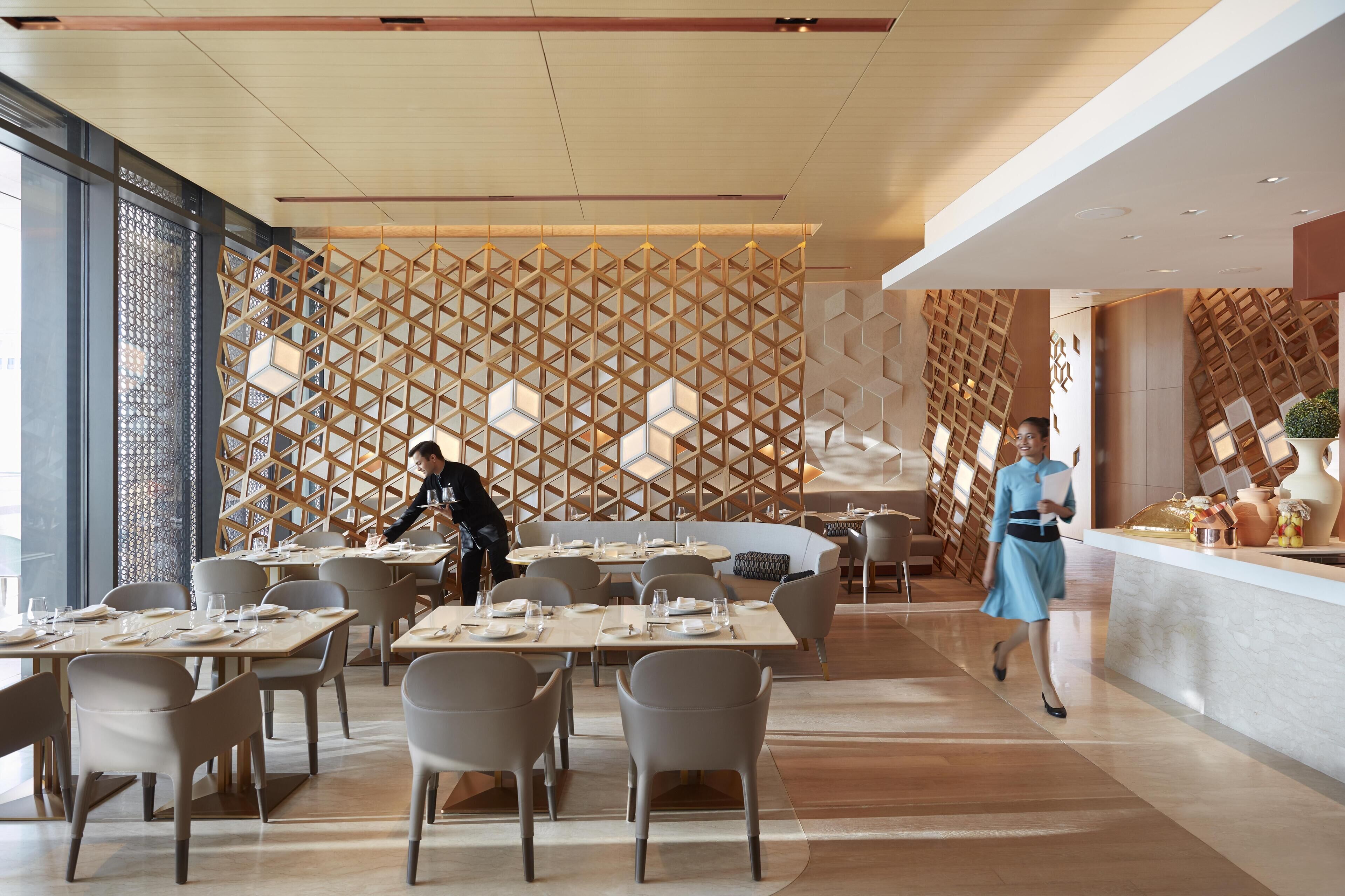 Un restaurante moderno con un diseño geométrico en una pared de madera, mesas dispuestas para comer y una zona de bar.