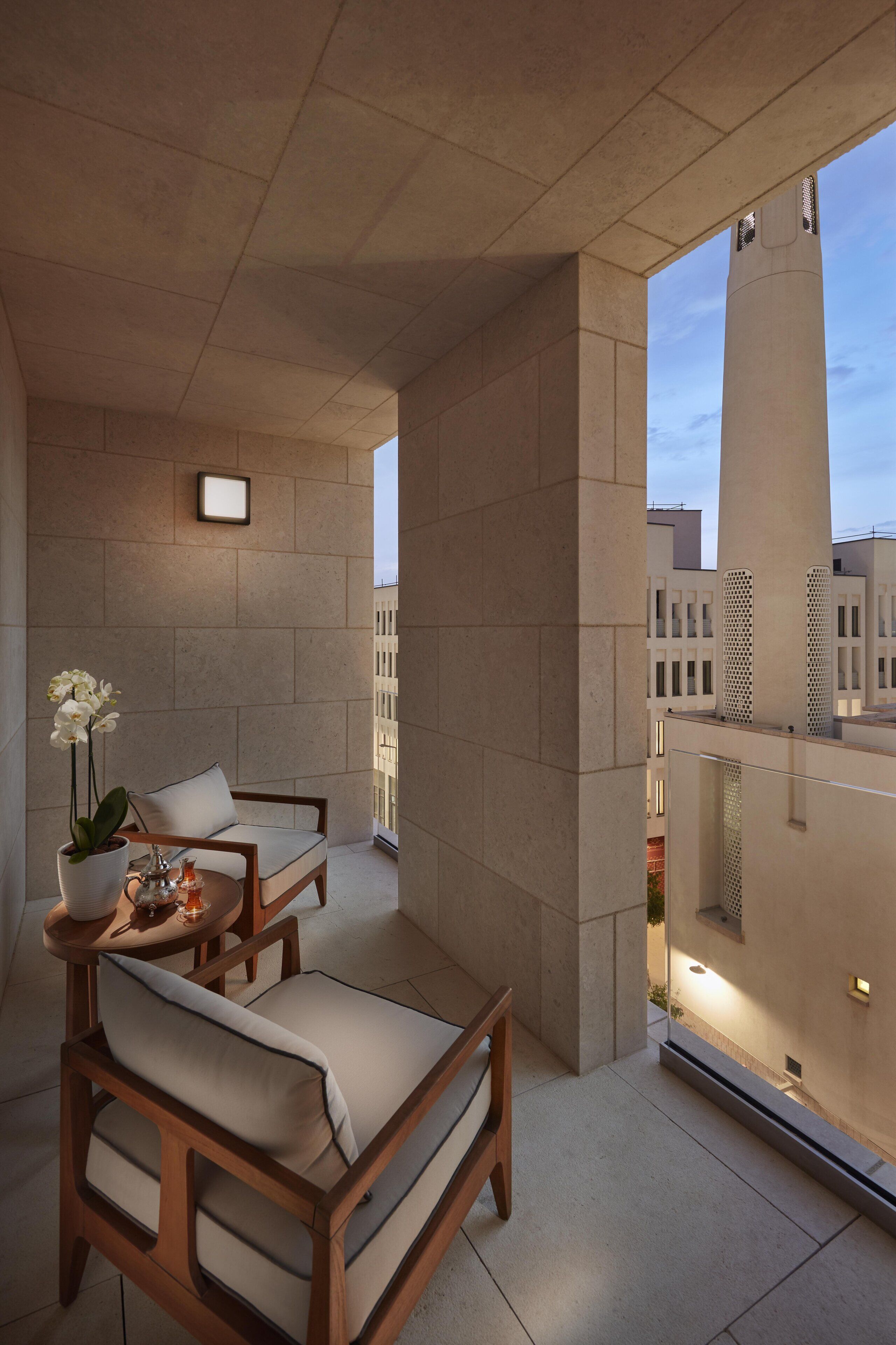 Un espacio al aire libre moderno con un sofá y sillones, una planta en maceta y una mesa con una jarrón y vasos.