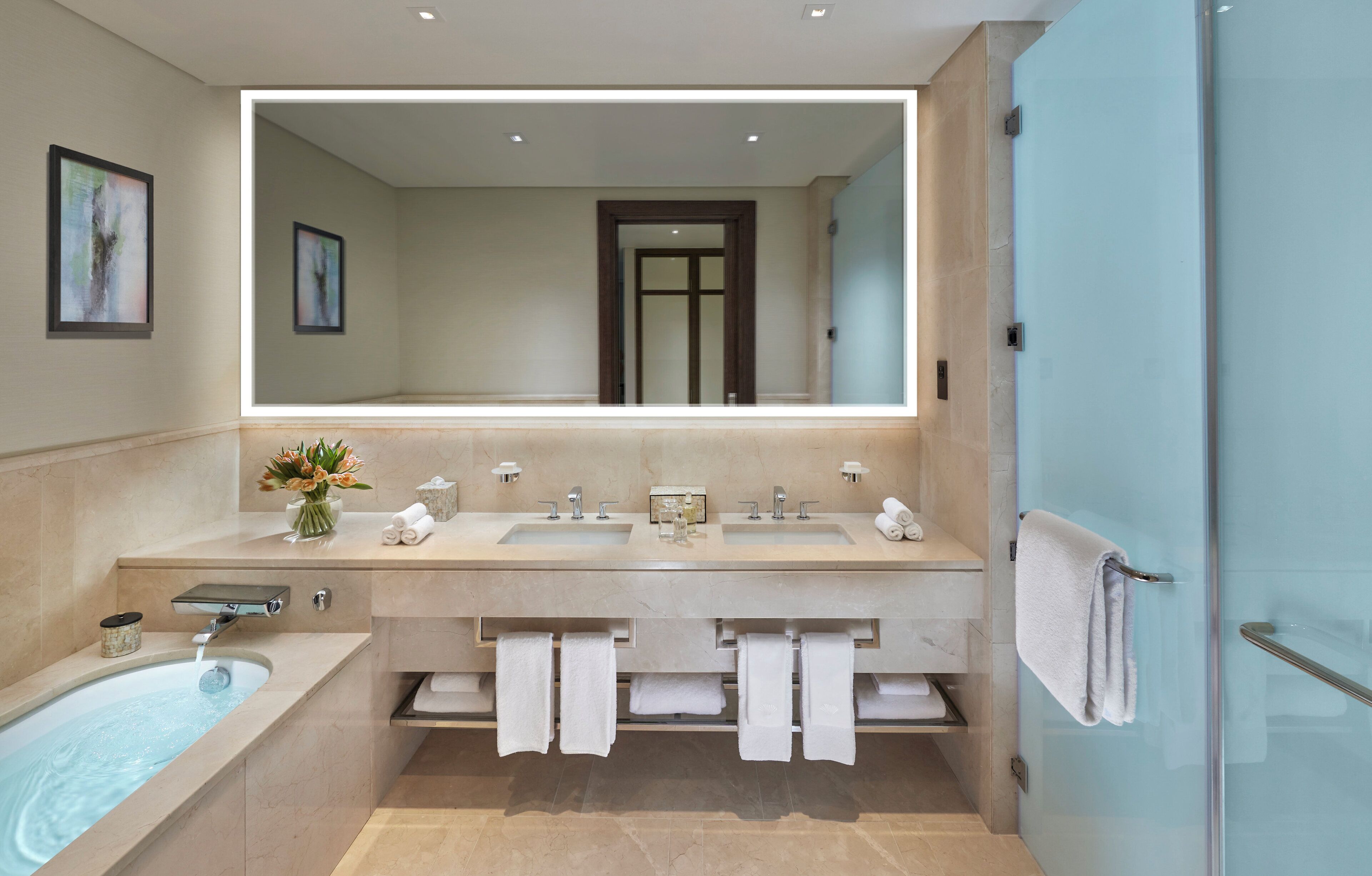 Un baño moderno con un espejo grande, lavamanos dobles, una bañera y un box de ducha de cristal.