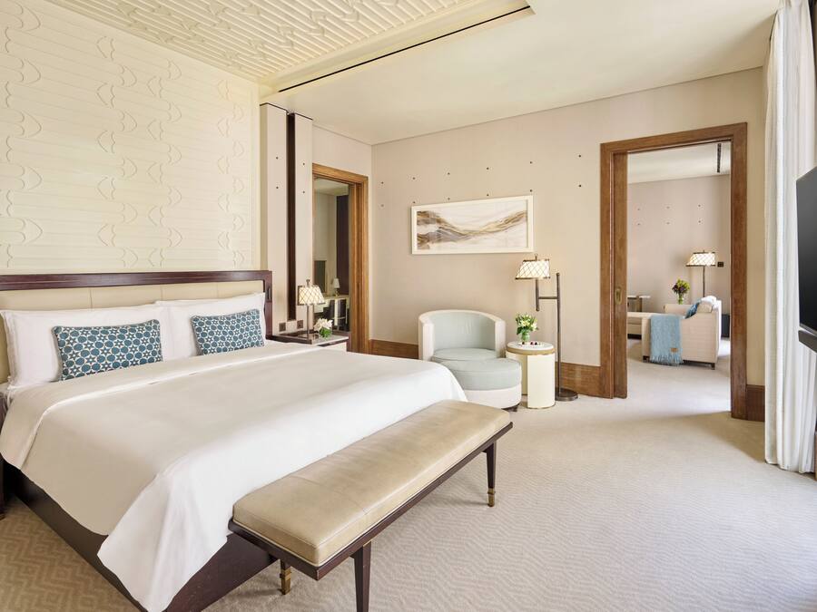 A hotel room with a large bed, a bench, a desk, a chair, a TV, and a mirror.