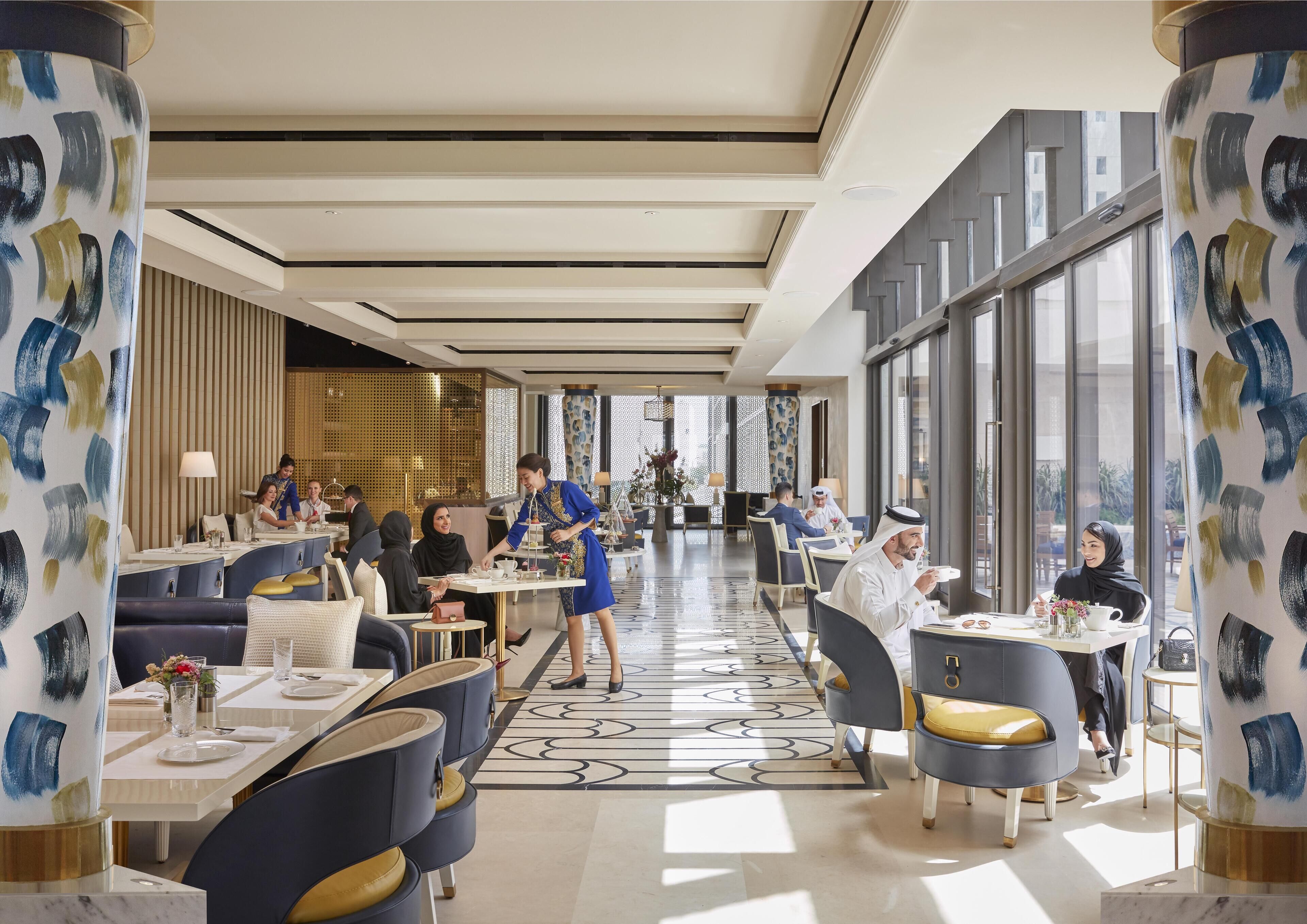 Un moderno hall de hotel con una zona de estar central, ventanas amplias y columnas decorativas.