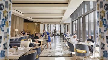 Un moderno hall de hotel con una zona de estar central, ventanas amplias y columnas decorativas.