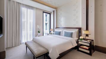 Habitación de hotel con una cama grande, una mesita de noche con lámpara, un banco y una ventana con cortinas.