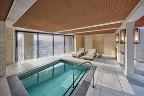 A modern indoor swimming pool with a wooden ceiling, tiled walls, and lounge chairs.