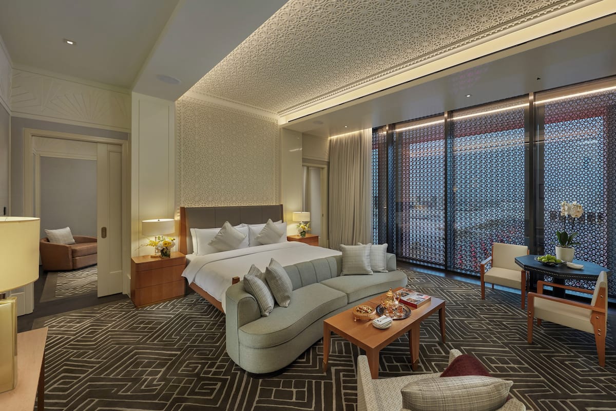 A hotel room with a large bed, a sofa, a coffee table, and a dining area.