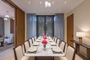 A dining room with a long table set for six, surrounded by chairs, with a decorative panel and curtains on the windows.
