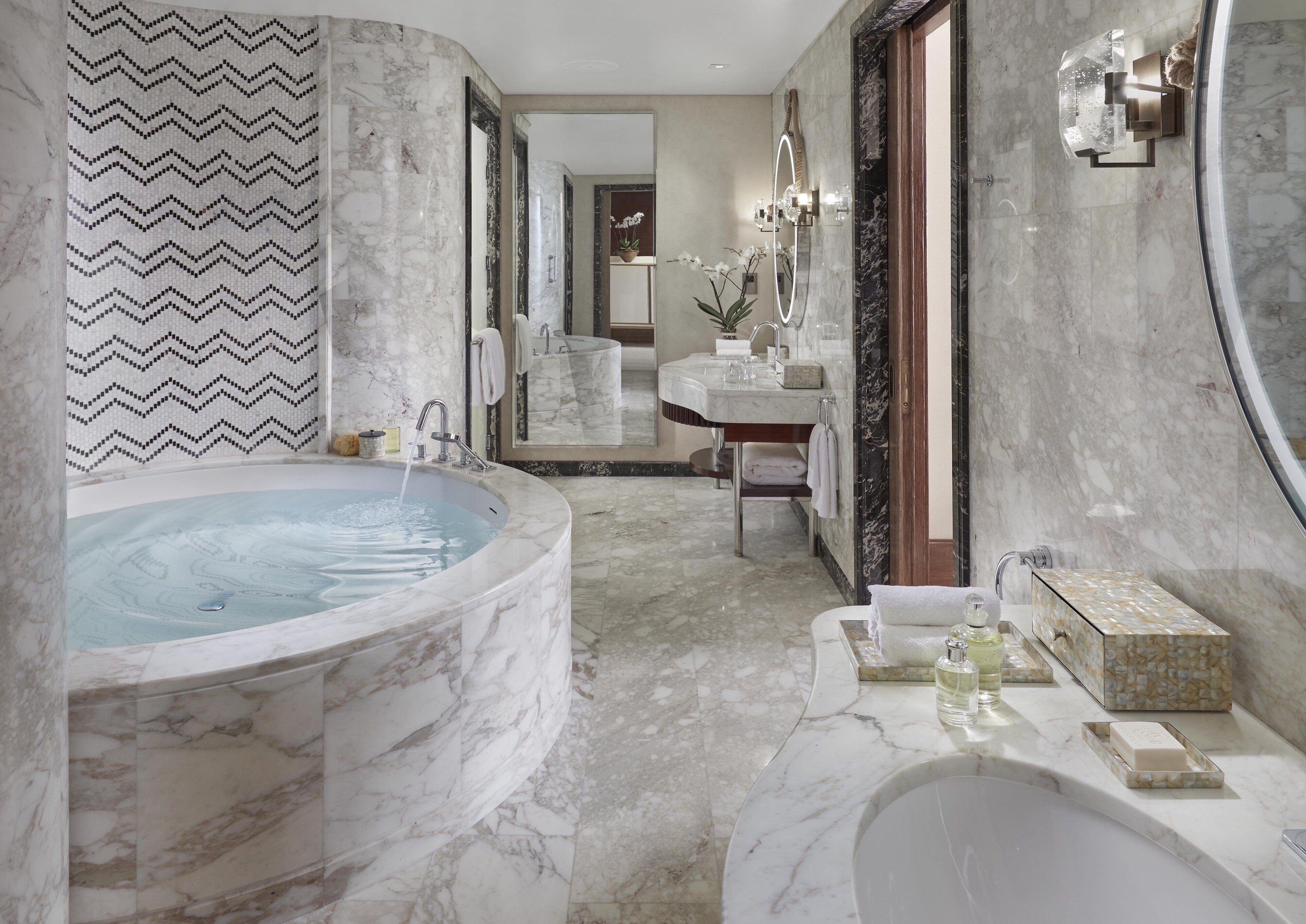 A luxurious bathroom with a large marble bathtub, a separate sink area, and a vanity with a mirror.