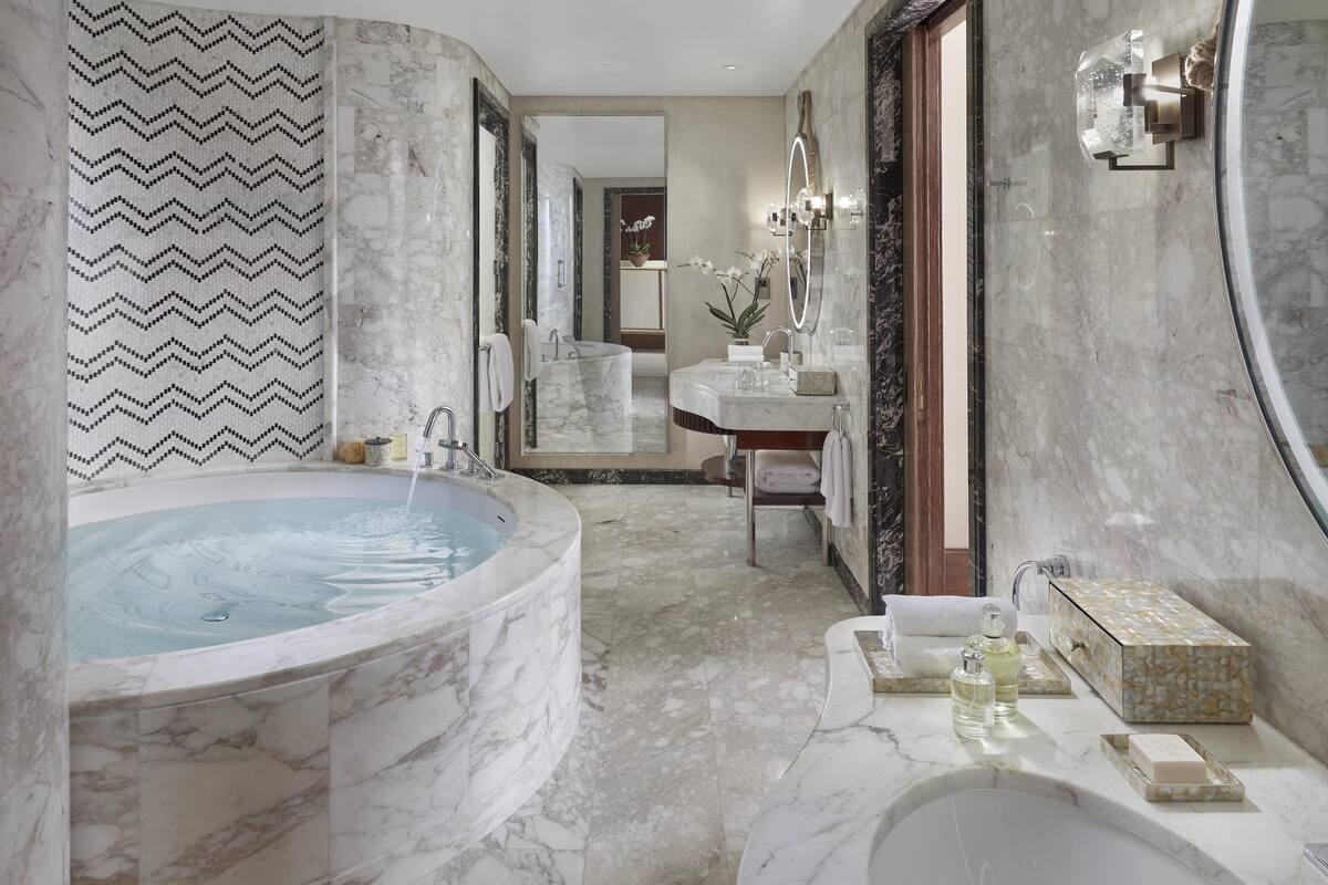 A luxurious bathroom with a large marble bathtub, a separate sink area, and a vanity with a mirror.
