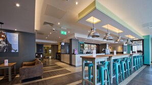 A modern bar area with a long counter, multiple bar stools, and pendant lighting. - Premier Inn Leeds Cc - Whitehall Road (Leeds)