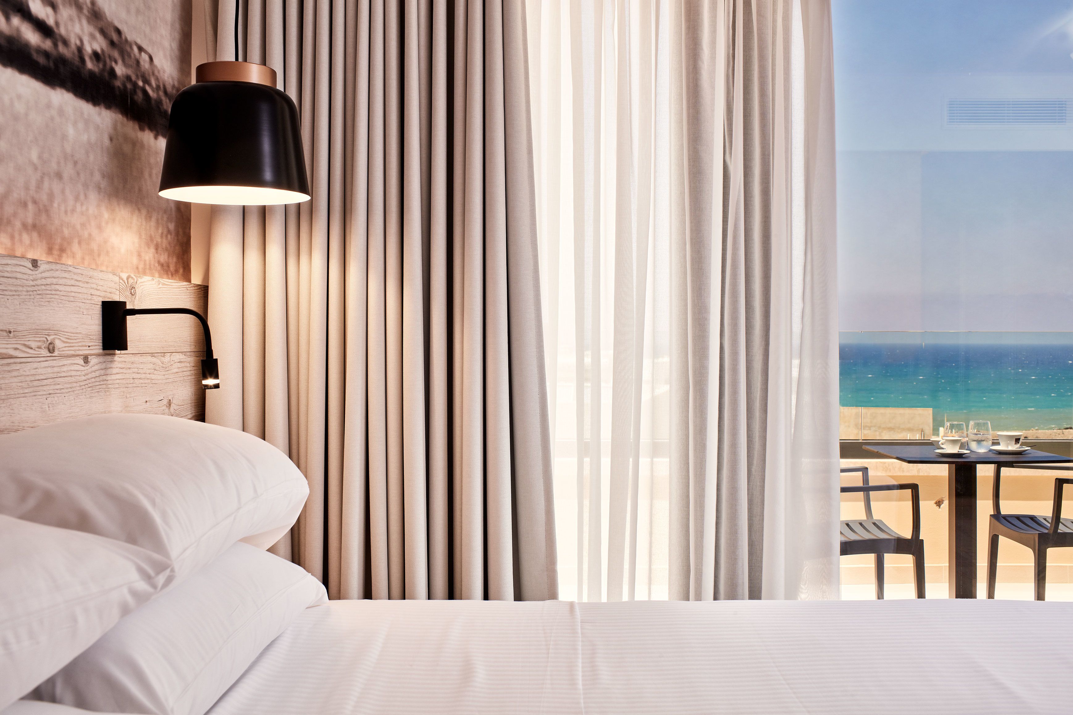 Habitación de hotel con cama, lámpara, cortinas y vista a la playa.