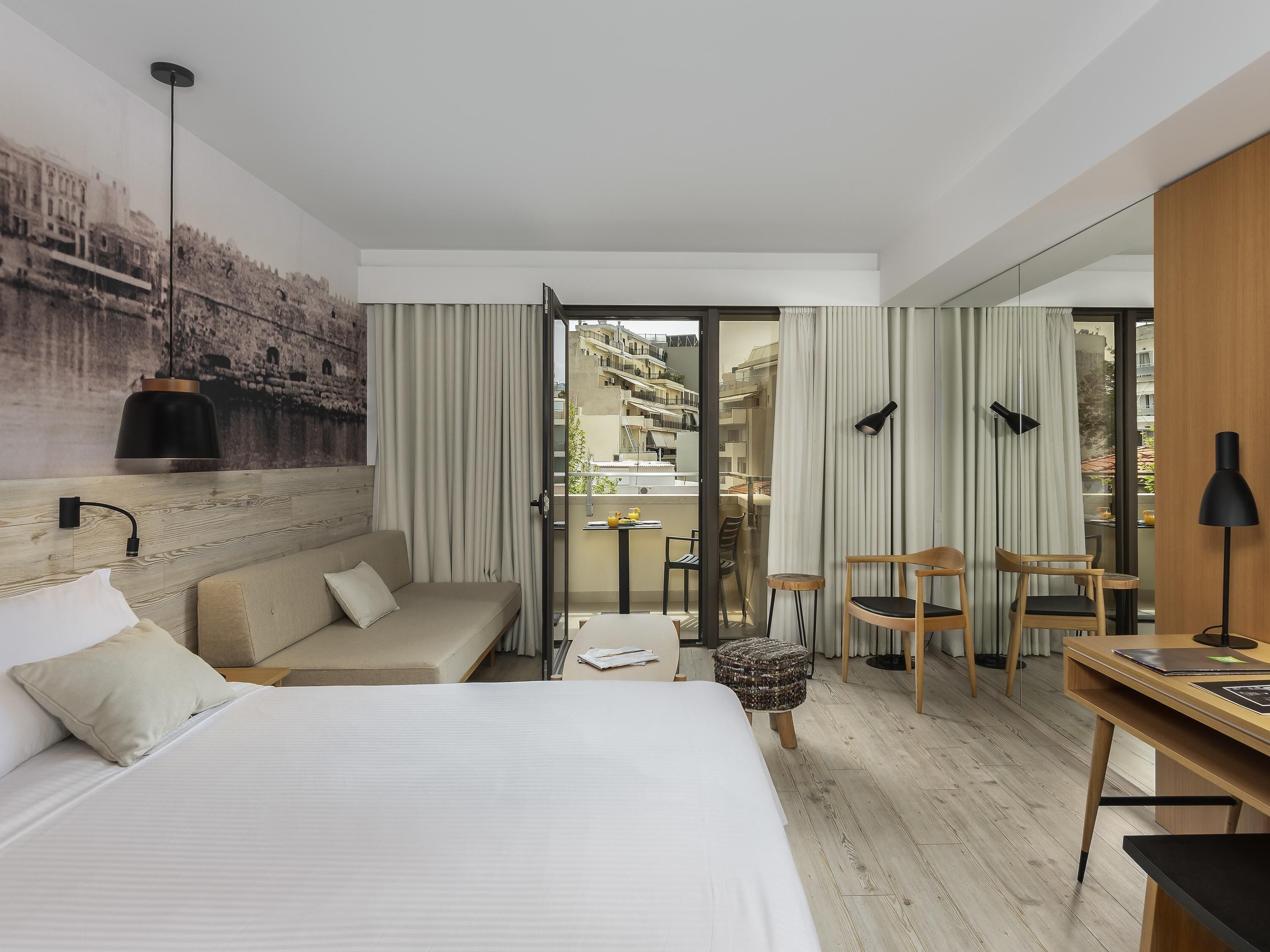 A hotel room with a bed, a sofa, a desk, and a view of the cityscape through the window.