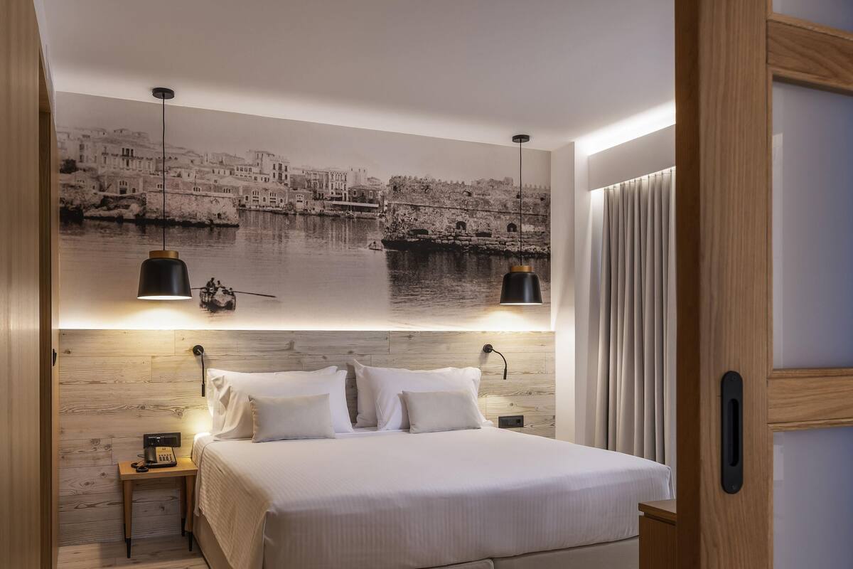 A bedroom with a large bed, two bedside tables, a wall-mounted lamp, and a mural of a coastal scene.