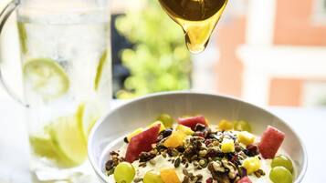 A bowl of yogurt topped with fruits and nuts, a glass of iced drink with lime, and a pitcher in the background.