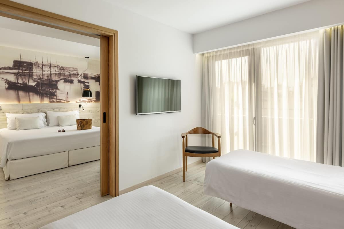 A hotel room with a bed, a chair, a TV, and a large window with curtains.