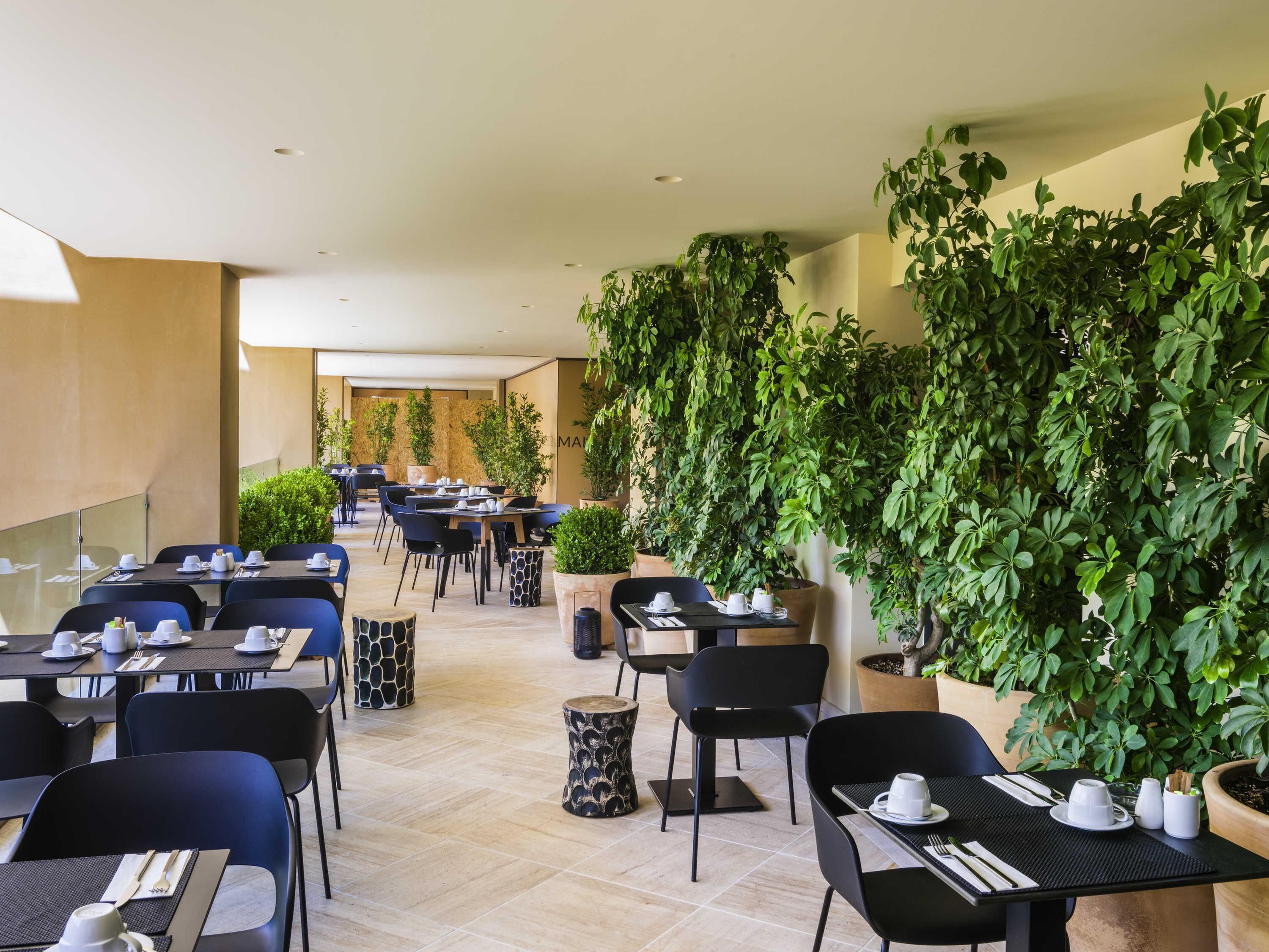 En modern restaurang med bord och stolar, krukväxter och ett rent, kaklat golv.