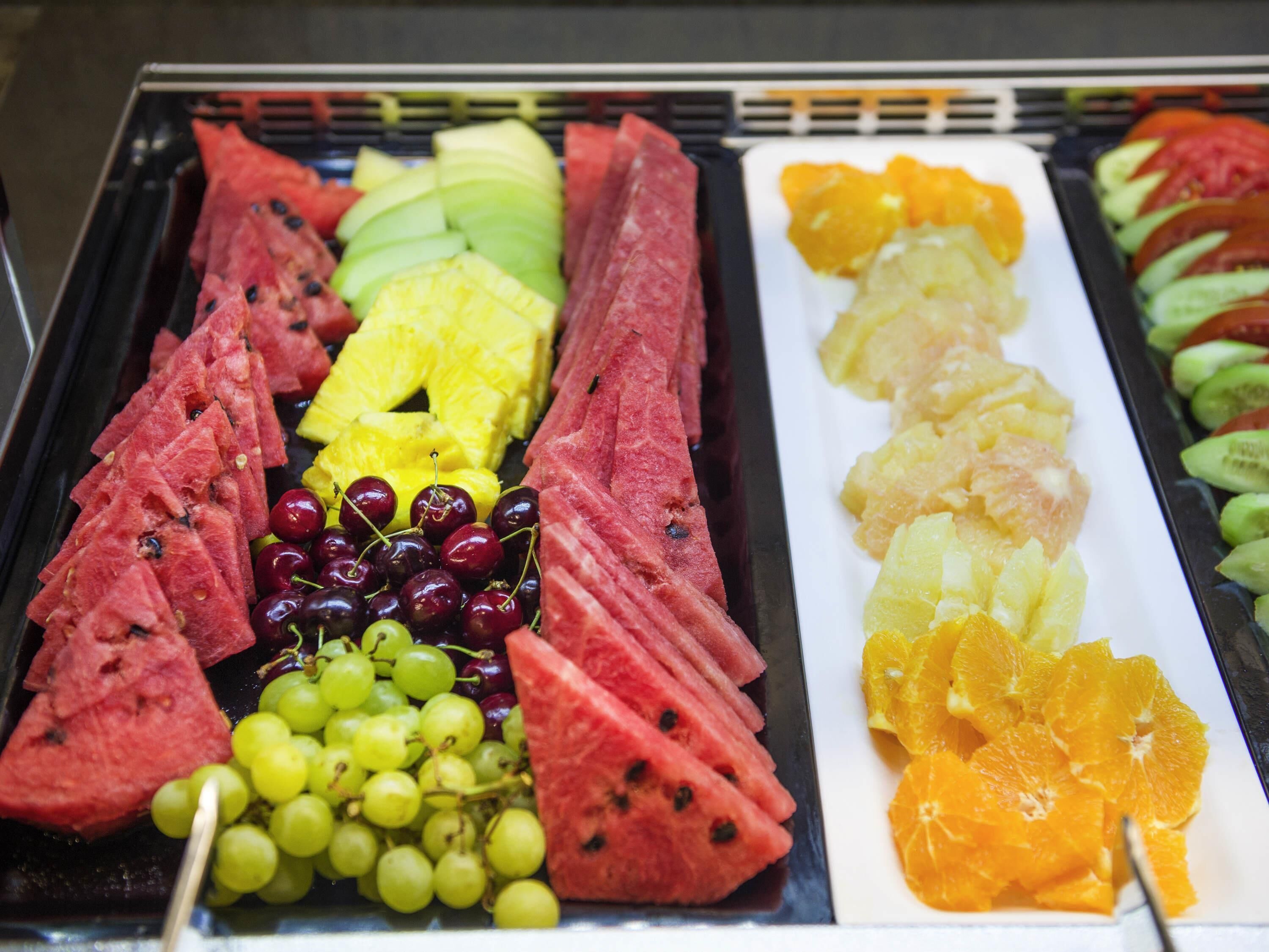 Una bandeja con frutas variadas como sandía, piña, uvas, cerezas y naranjas.