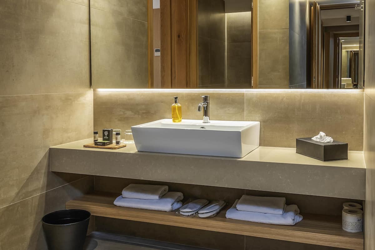 A modern bathroom with a white sink, wooden shelves, and a mirror.