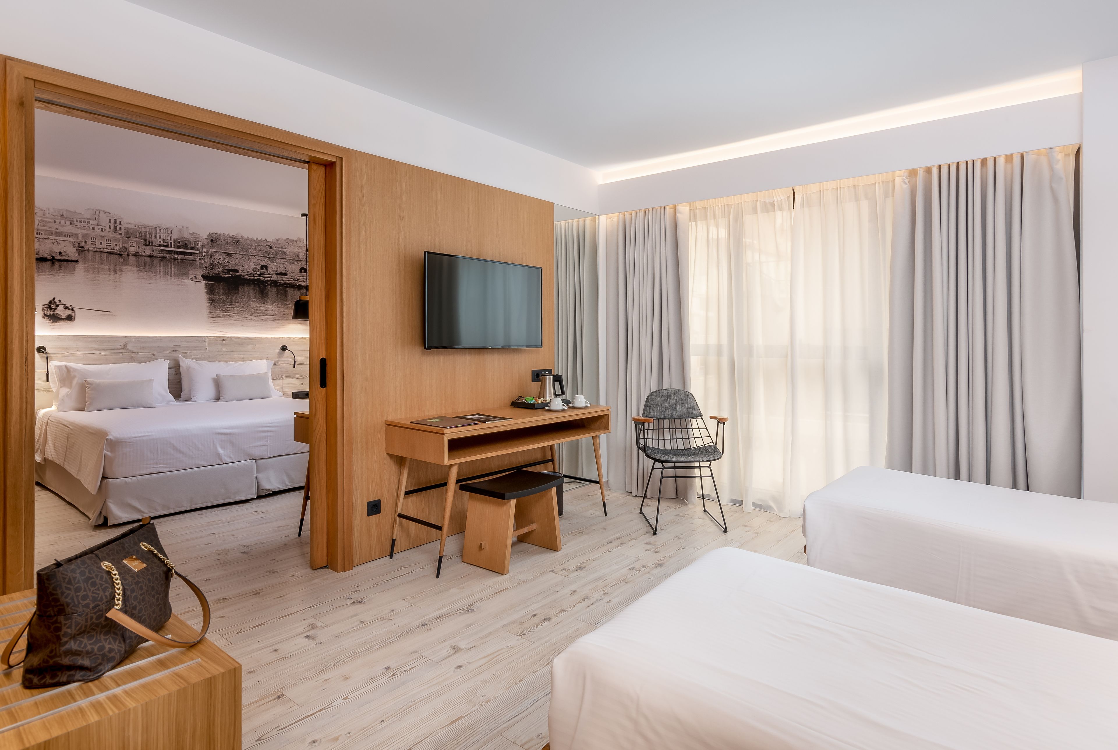 A hotel room with a bed, a desk, a chair, a TV, and a view of a river.