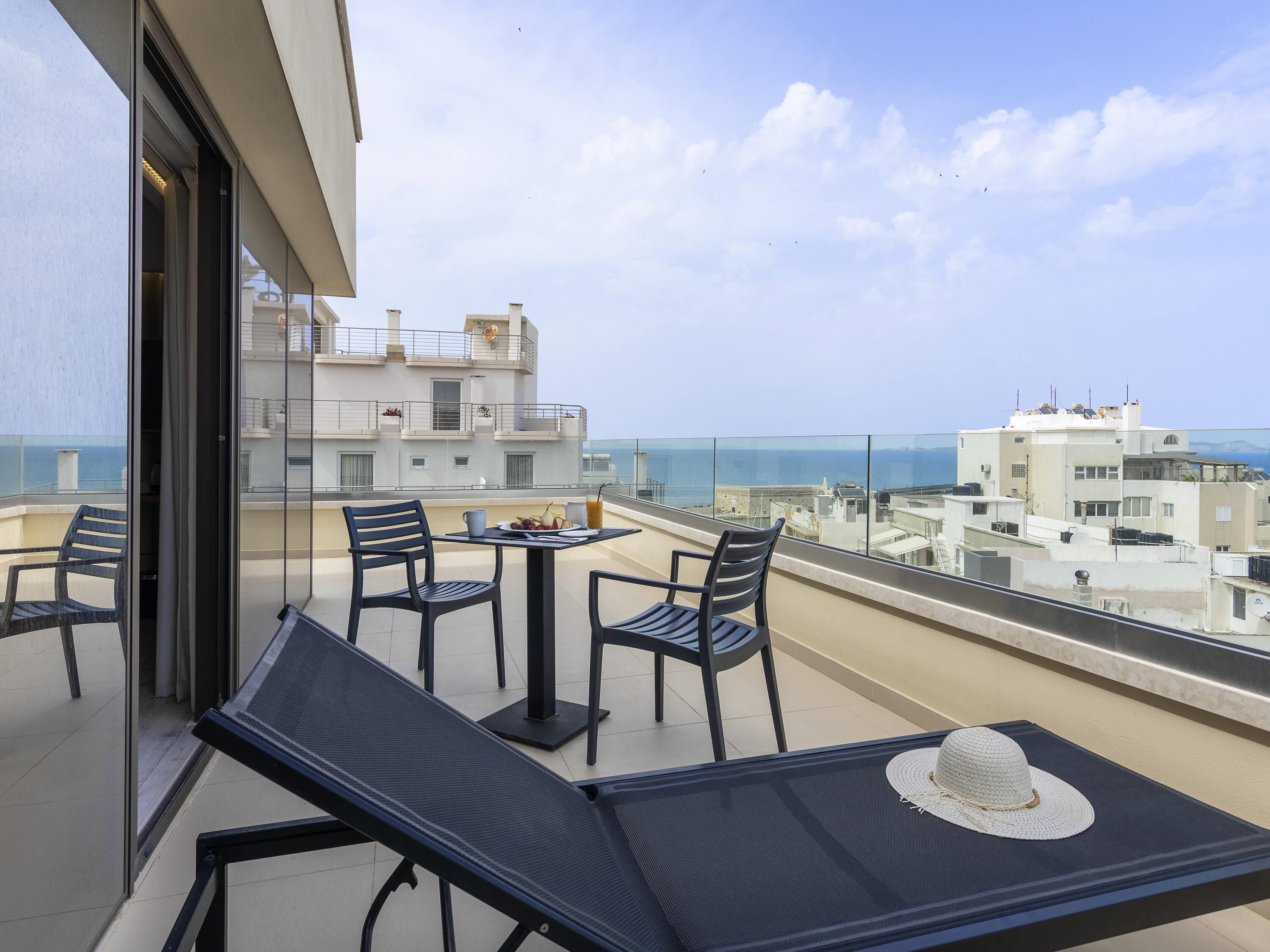 A balcony with a table set for two, chairs, and a hat on the table.
