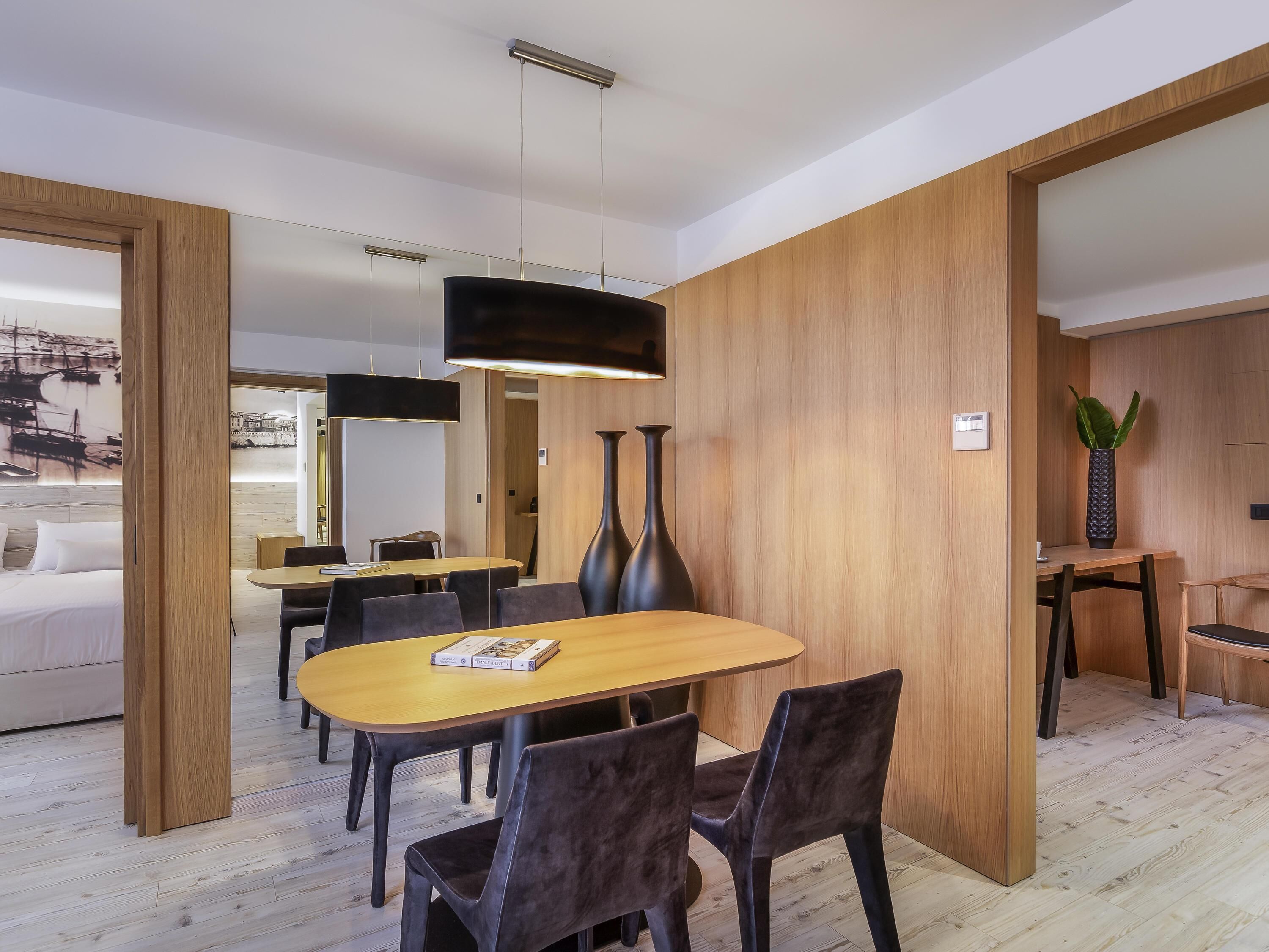A modern dining area with a wooden table and chairs, a large vase, and a hanging light fixture.