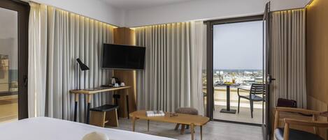 A hotel room with a bed, a desk, a TV, and a balcony with a view of the city.