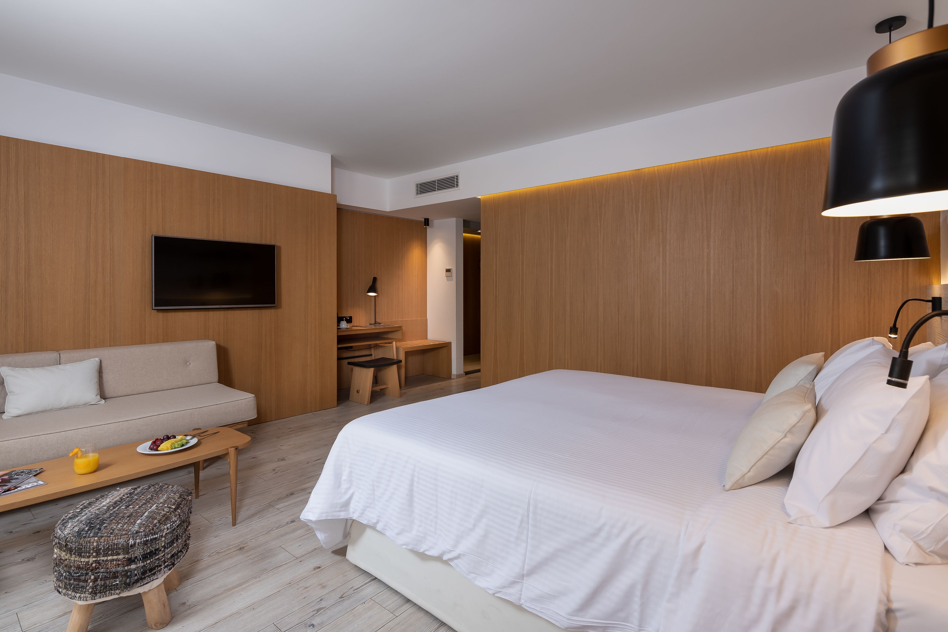 Ein modernes Hotelzimmer mit einem großen Bett, einer Couch, einem Schreibtisch und einem Fernseher.