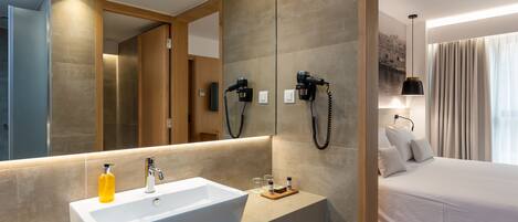 A modern hotel room with a large mirror, a white sink, and a bed with white linens.