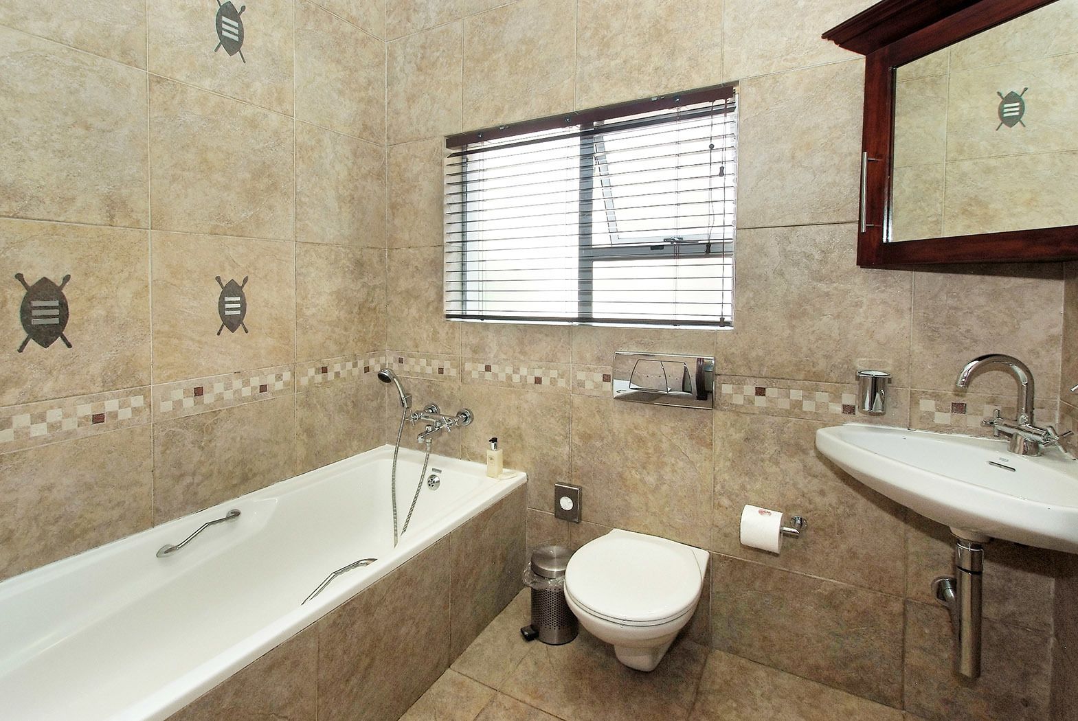 Une salle de bain équipée d’une baignoire, de toilettes et d’un lavabo, avec des murs carrelés et une fenêtre.