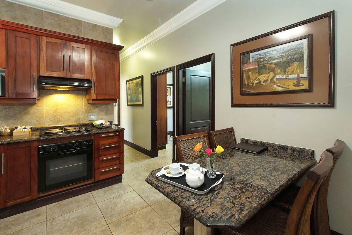A kitchen with wooden cabinets, a built-in oven, and a granite countertop. There is a dining table with chairs and a vase of flowers.