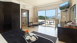 Ett hotellrum med en säng, en matplats, en TV och en balkong med utsikt över havet.