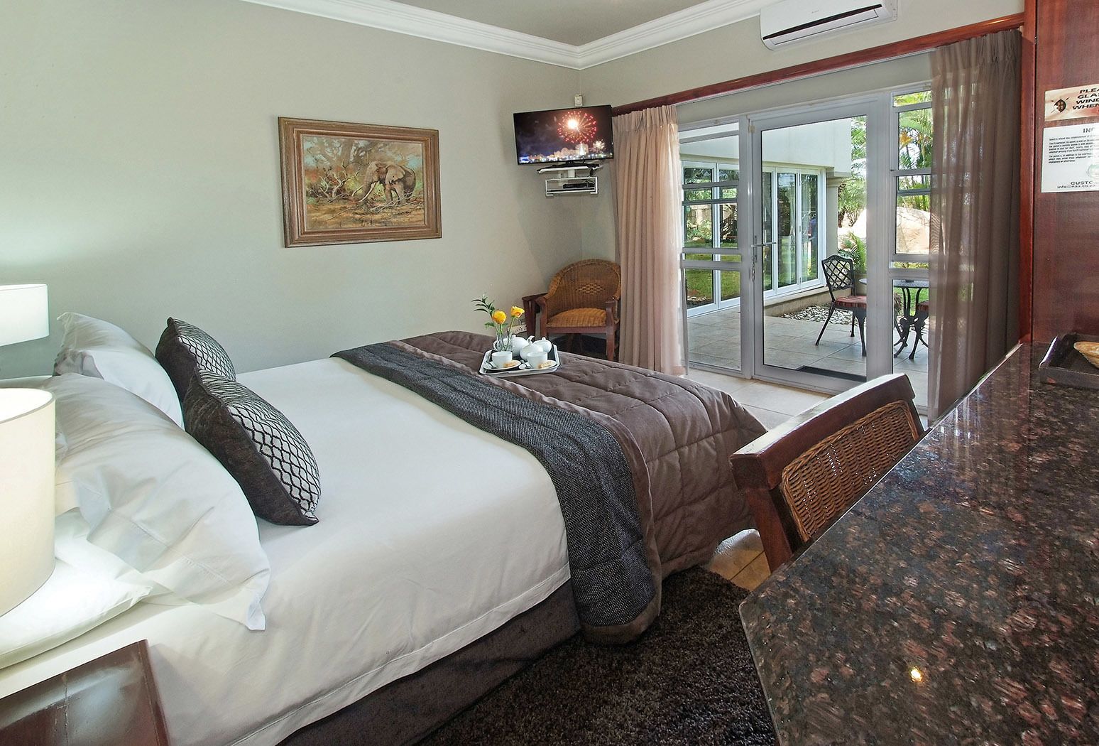 A hotel room with a bed, a TV, a painting, and a view of the outside.